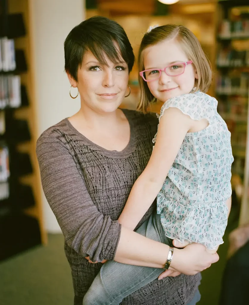 Frau, die ein Kind auf dem Arm hält. Beide schauen in die Kamera.